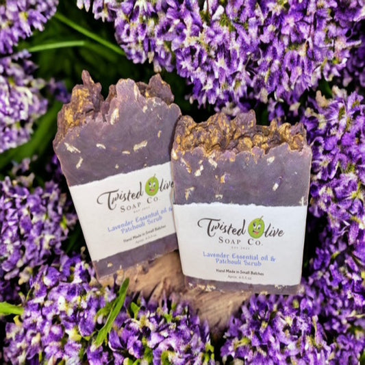 Two  violet soap bars from Twisted Olive Soap Co. surrounded by lavender flowers. The soap has ingrained oatmeal as a loofah. 