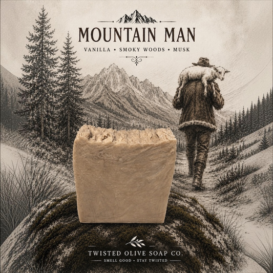 A rectangular bar of soap stands on a rock in front of a sepia-toned mountain landscape illustration. Text at the top reads 'MOUNTAIN MAN' with notes 'VANILLA • SMOKY WOODS • MUSK,' and the bottom reads 'TWISTED OLIVE SOAP CO.  Smell Good. Stay Twisted is the slogan at the bottom
