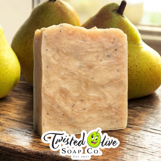 A bar of soap with a texture that looks speckled with small black seeds, placed on a wooden surface with fresh pears in the background. Twisted Olive Soap Co. logo is on the bottom